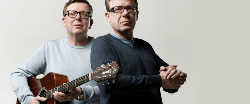 Two men in glasses posing with a guitar